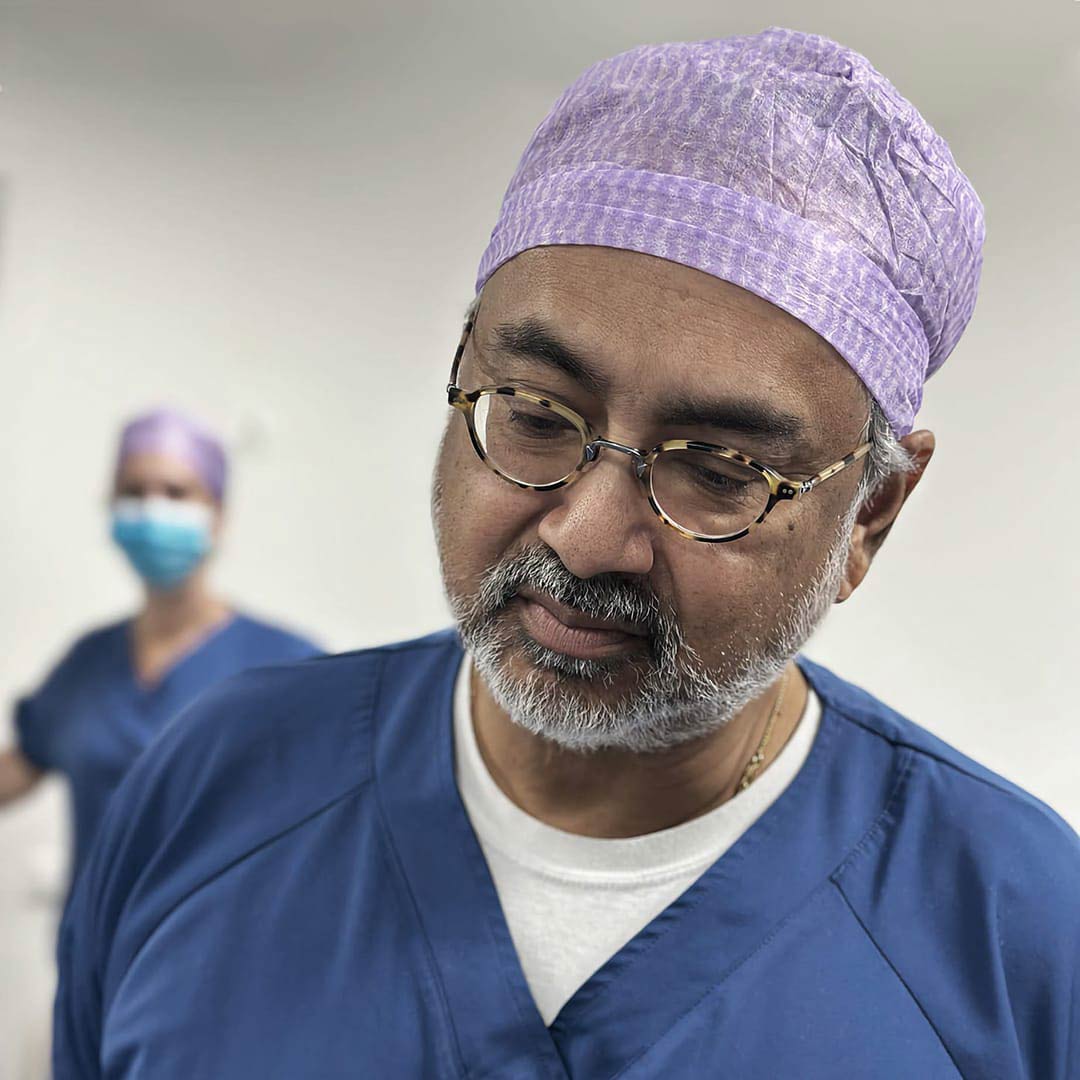 Dr. Refaat Karim van ReSculpt Aesthetics kijkt aandachtig naar de uitvoering van een cosmetische behandeling. Hij heeft zijn operatie kleding aan.